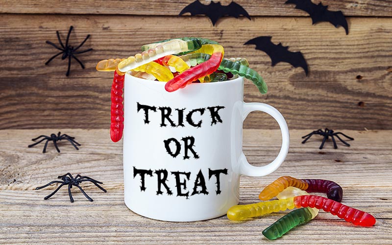 White mug filled with gum worms and text on it with halloween elements behind